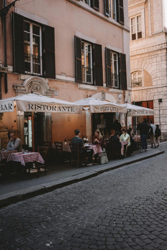 pexels-photo-17649415-17649415 Quaint outdoor dining scene at a traditional Roman restaurant on a cobblestone street.